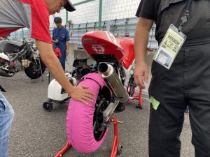 暖気場でバイクのリアタイアの温まり具合を手で触って確認するMさん。